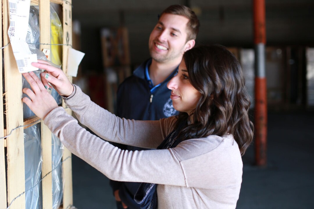 A man and woman smiling while working in a warehouse together. They are applying labels to boxes of product.